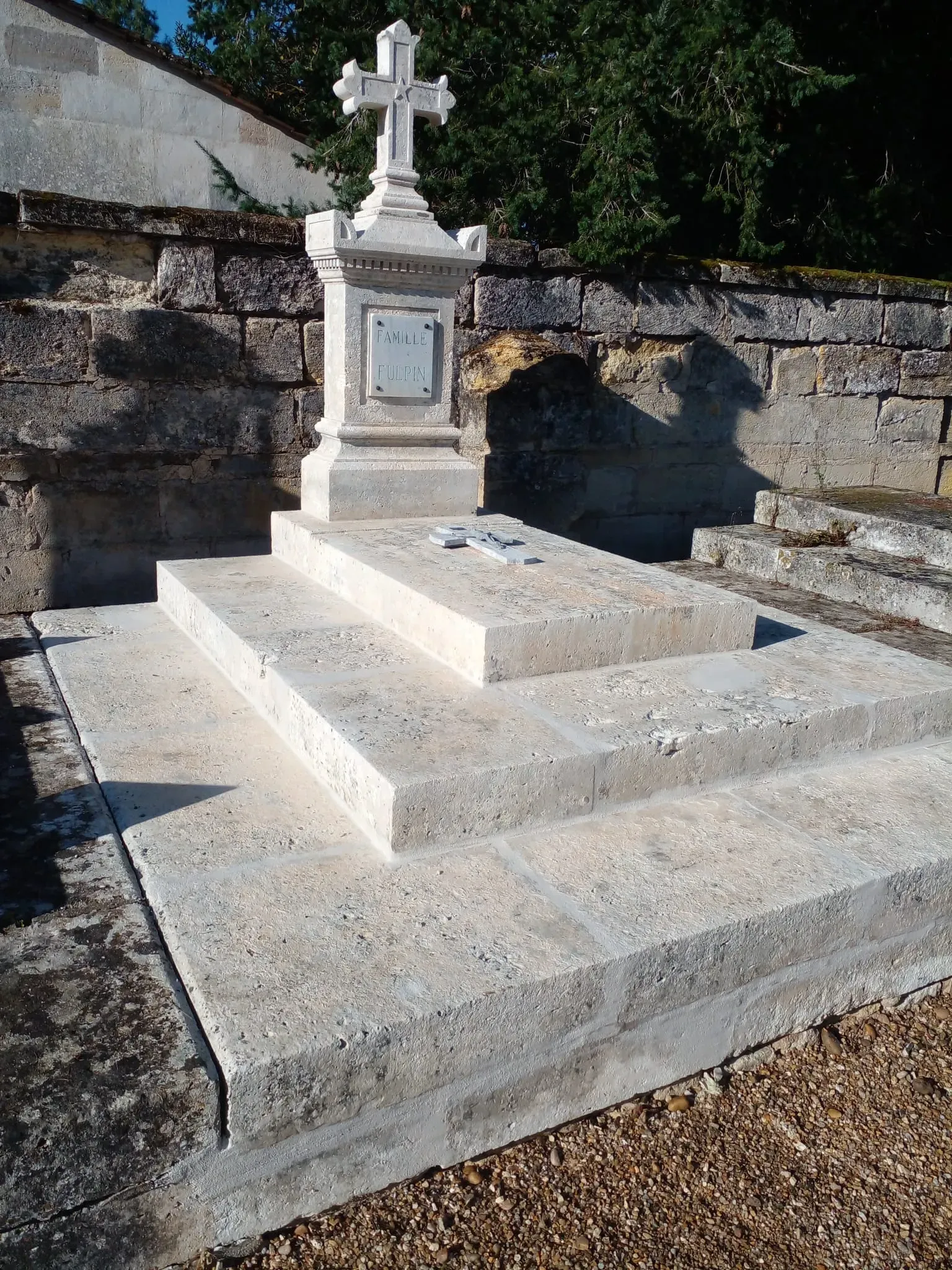 Tombe ancienne en pierre sculptée surmontée d'une croix chrétienne dans un cimetière.