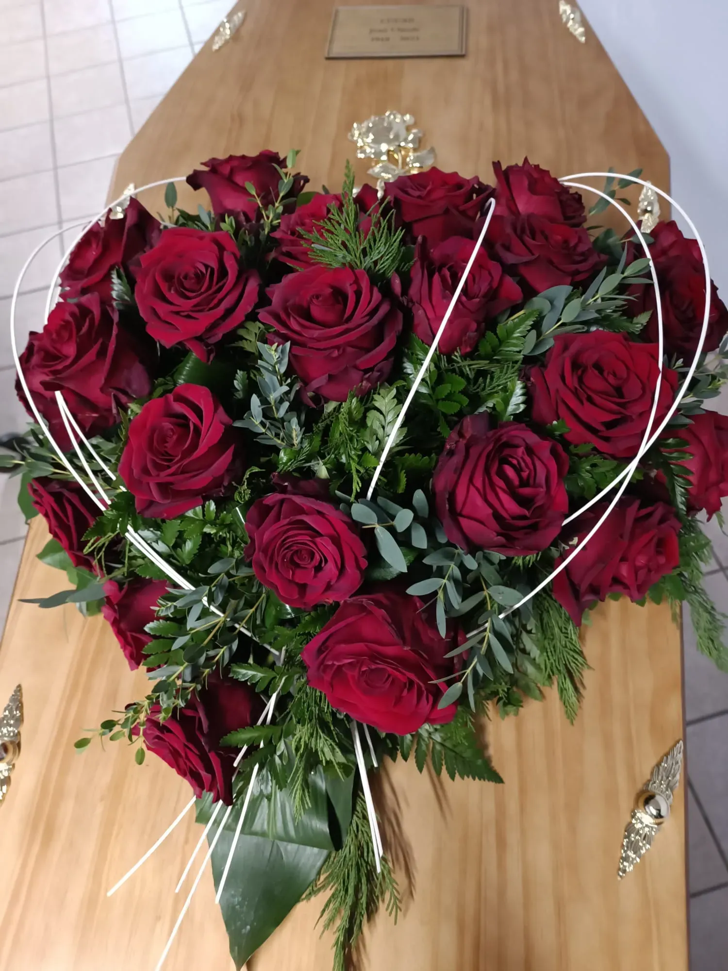 Grand bouquet en forme de cœur composé de roses rouges posé sur un cercueil.
