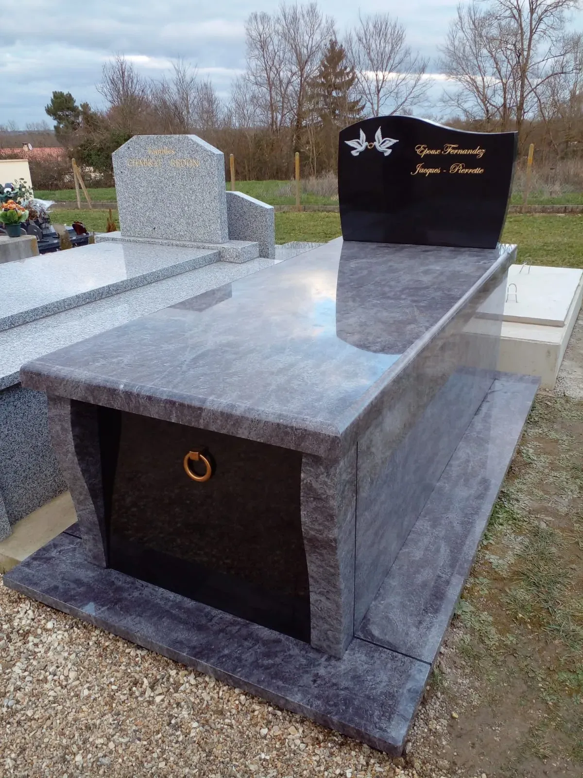 Monument funéraire moderne en granit gris foncé et stèle en marbre noir gravée.