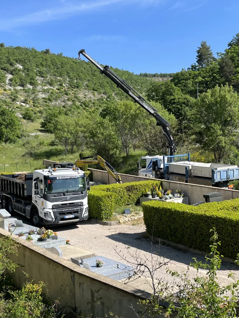 Camion-grue de marbrerie funéraire en cours d'intervention dans un cimetière paysager.