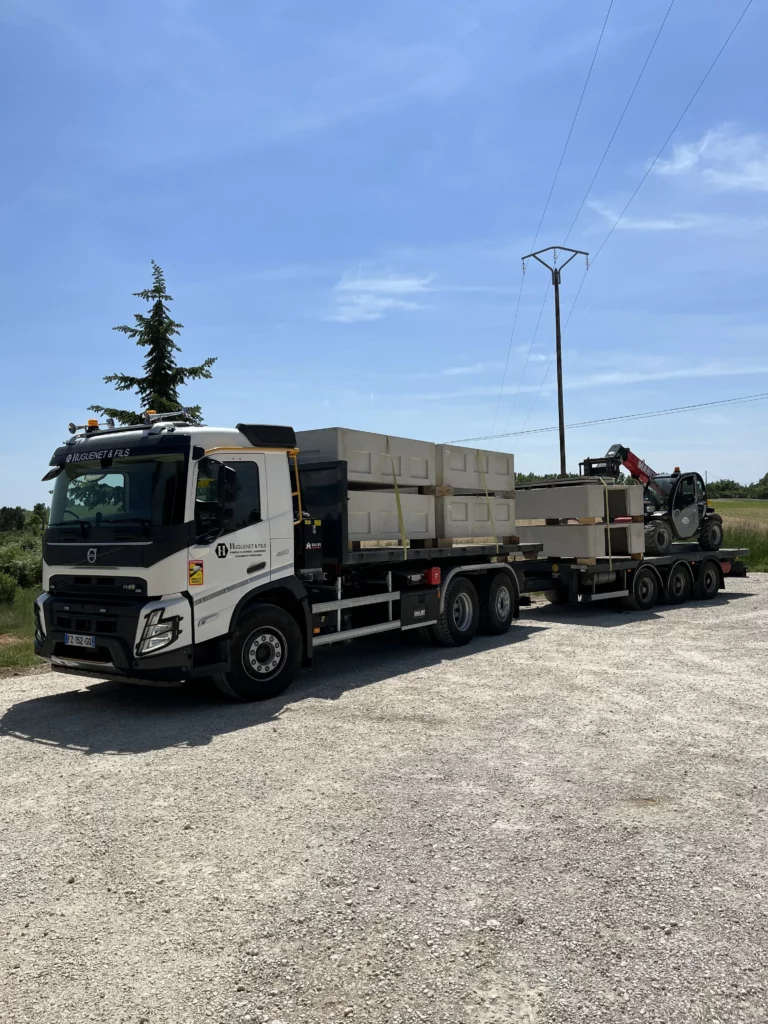 Camion poids lourd transportant des cav caveaux funéraires en béton sur sa remorque.