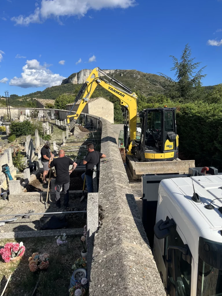 Chantier de terrassement dans un cimetière avec une mini-pelle Yanmar et des marbriers.